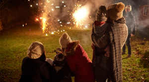 Two young families standing outside in garden on cold, dark night, watching fireworks together